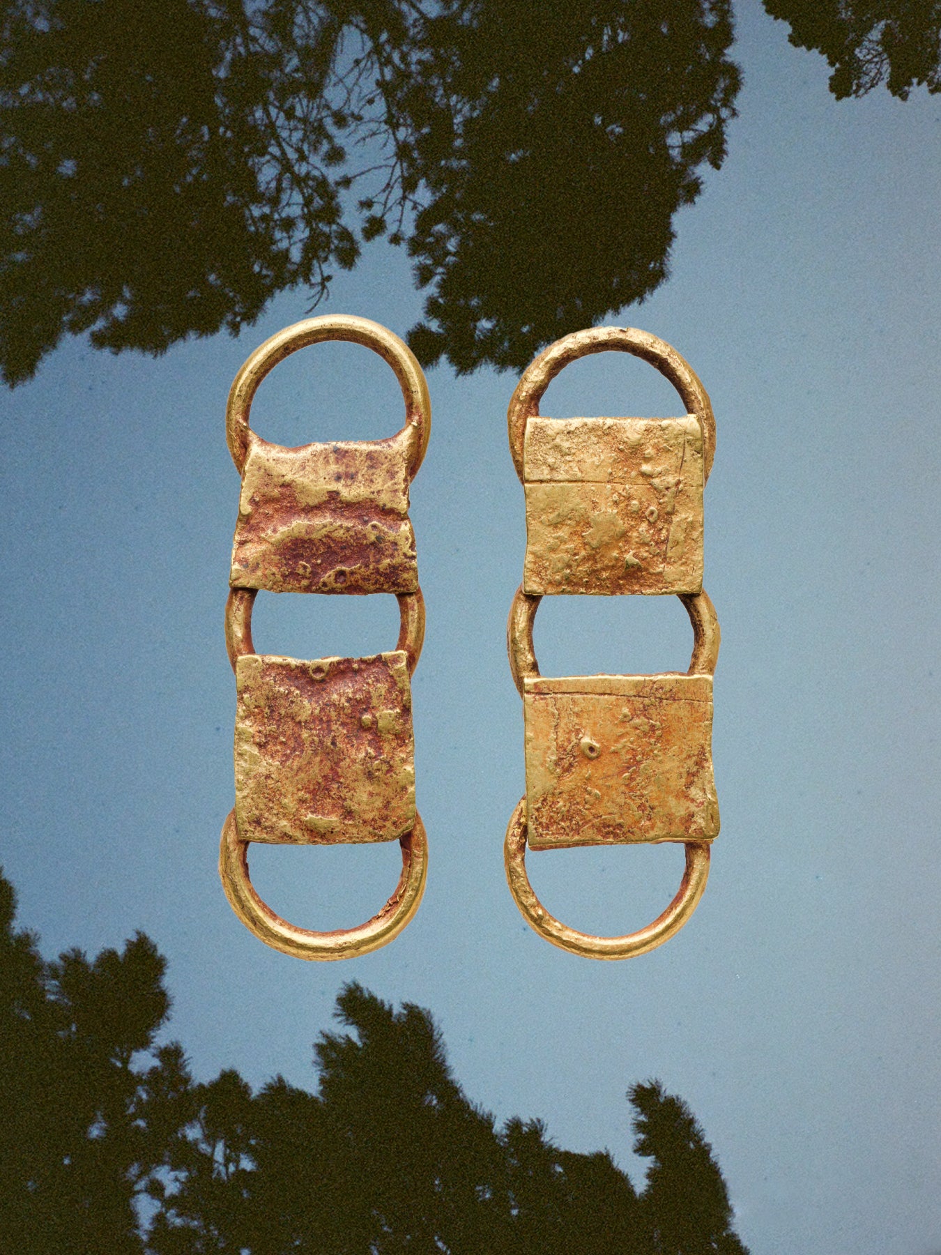 Pair of gold earrings against a blue sky with tree silhouettes