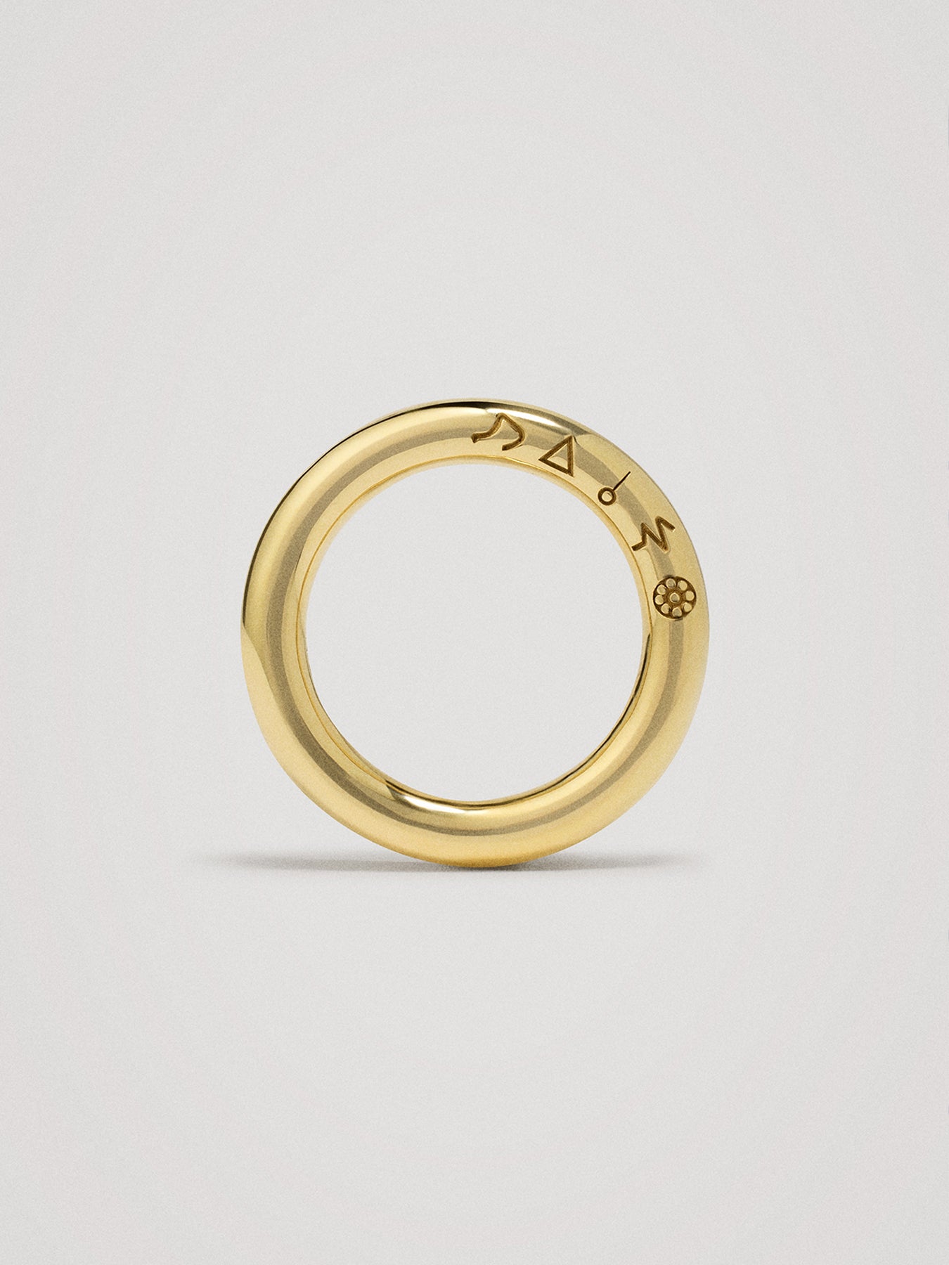Gold ring with engraved symbols on a light gray background