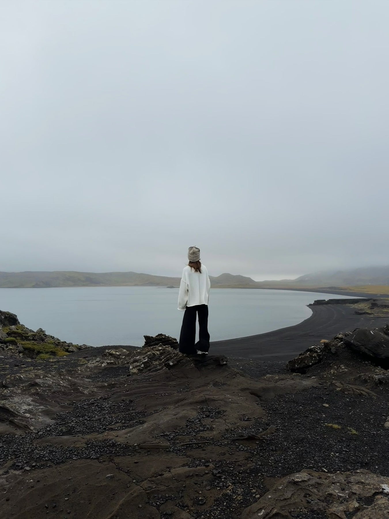Person standing on a rocky landscape with a body of water and mountains in the background