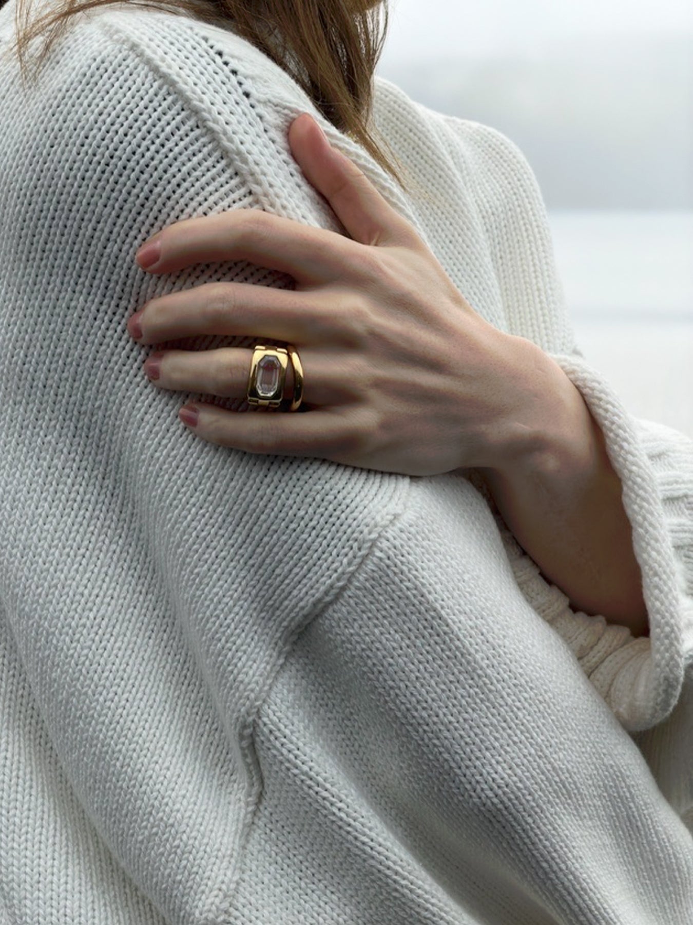 Hand wearing a gold and diamond ring on a white sweater