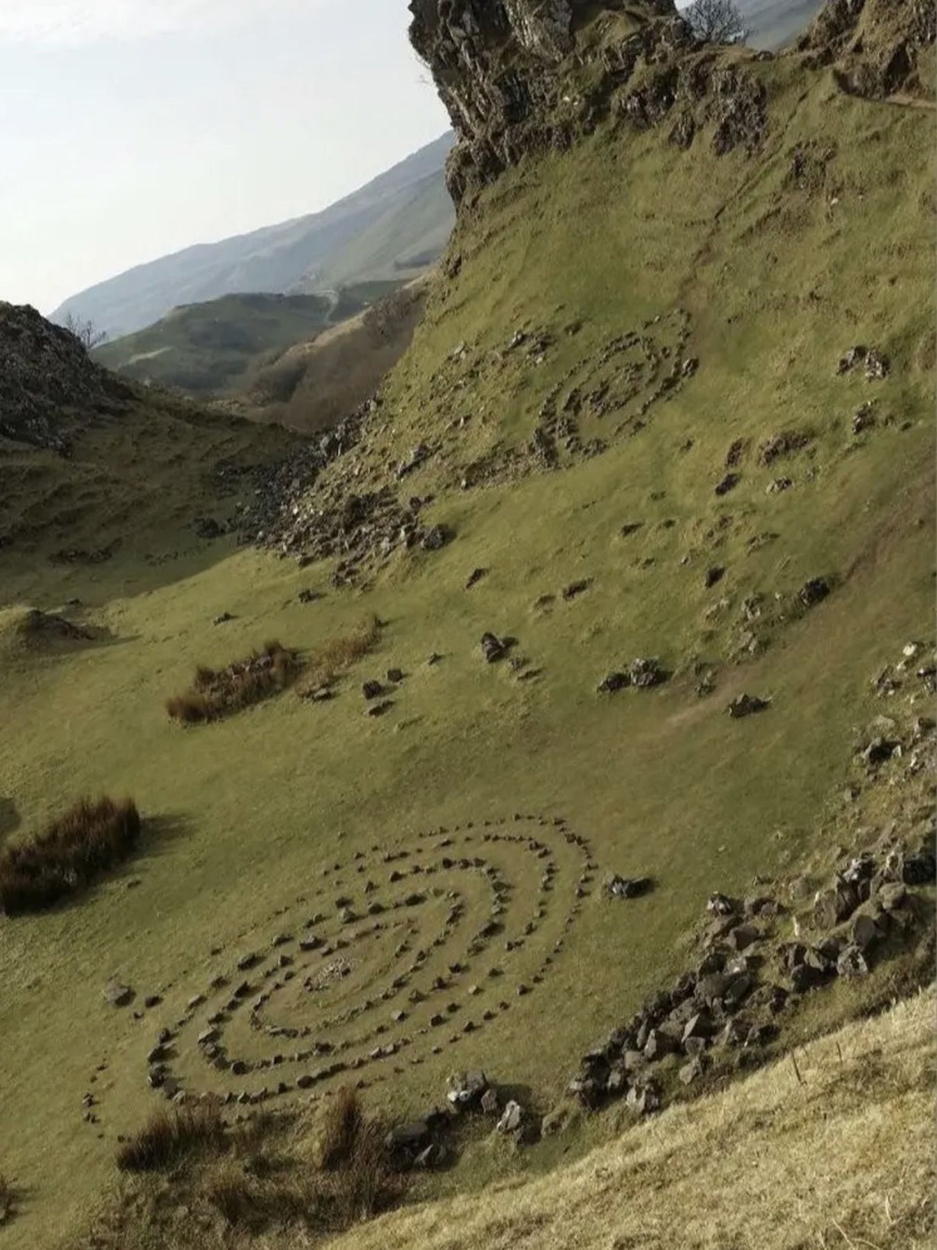 Concentric circles of stones on a grassy hillside with mountains in the background