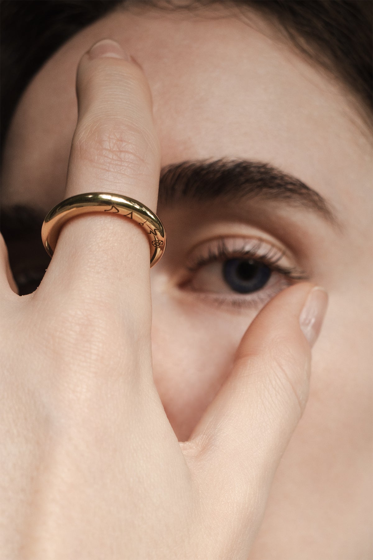 Close-up of a hand with a gold ring covering one eye