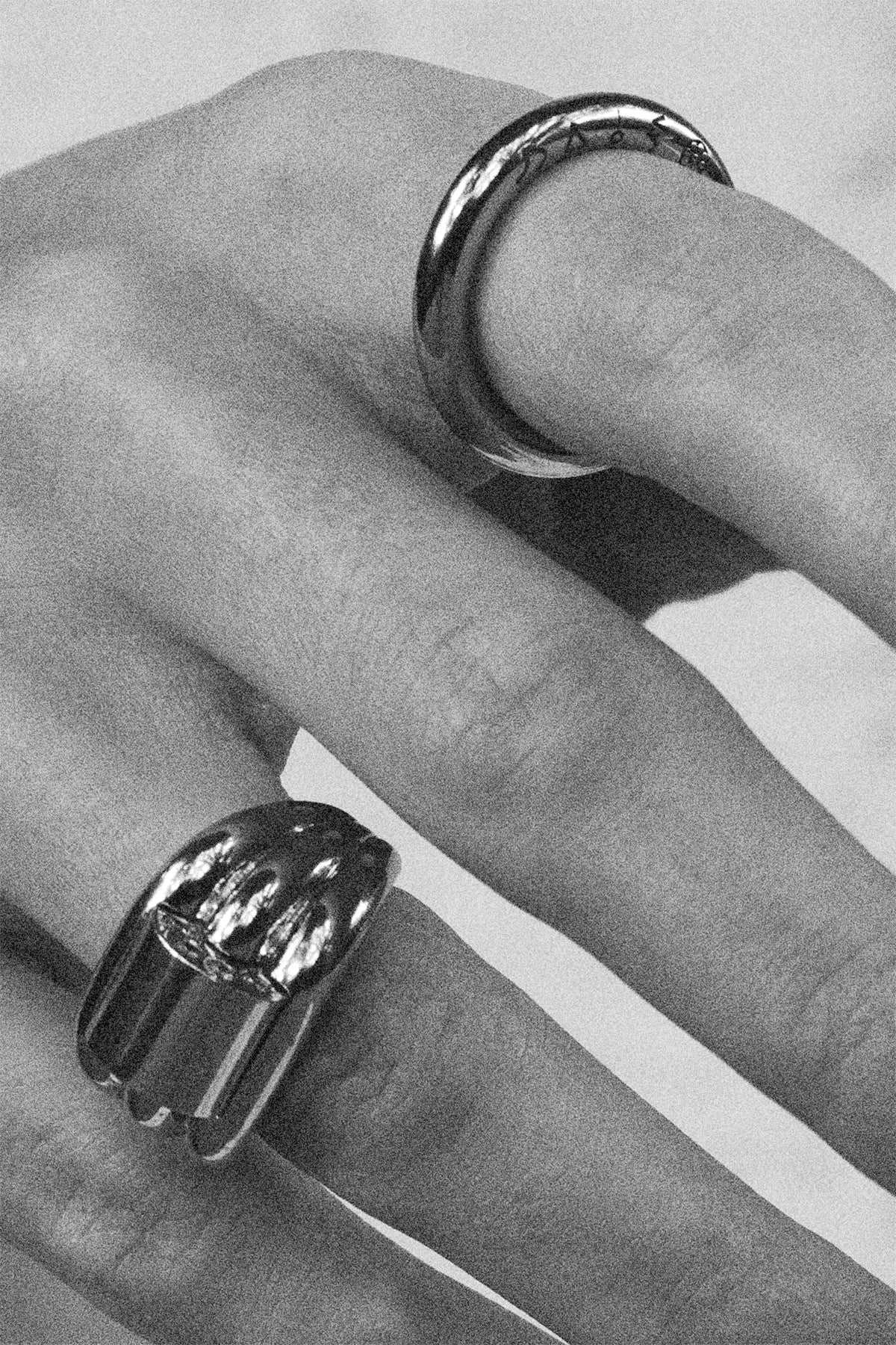 Close-up of a hand wearing two gold rings on a light background