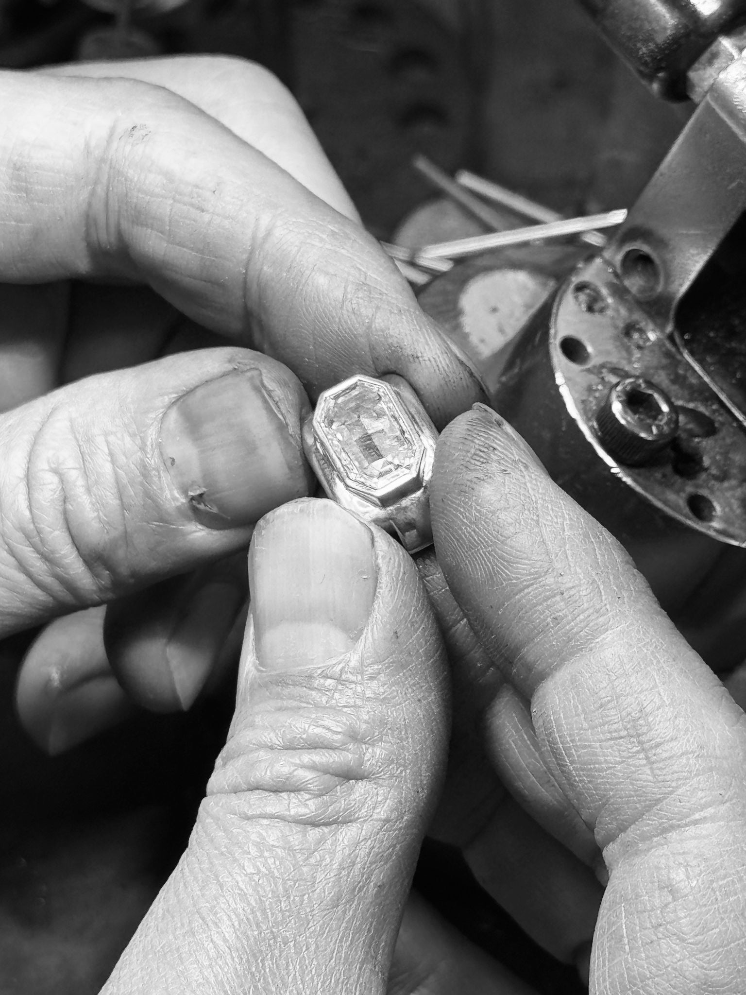 Close-up of jeweler’s hands holding our memo ring with a portrait diamond next to a jewelry tool