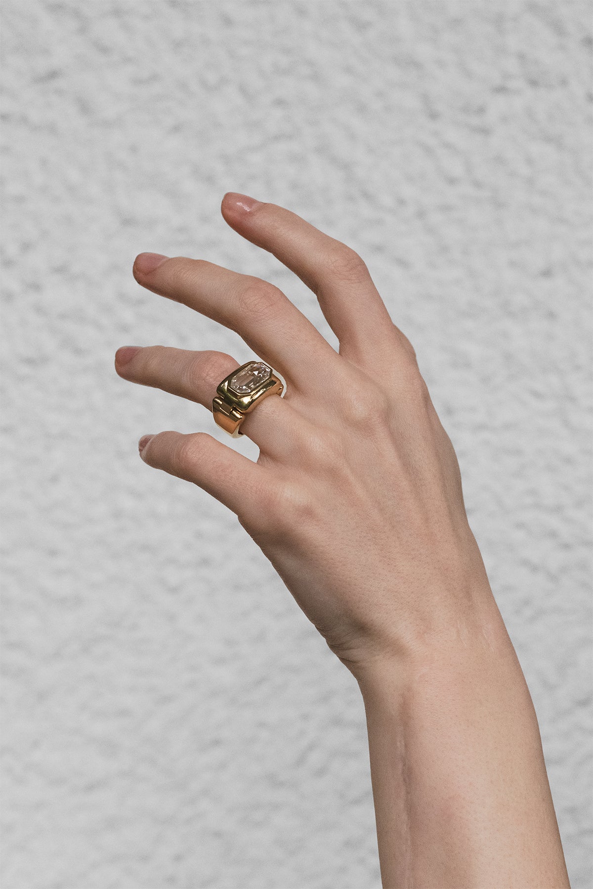 Hand wearing a gold ring on a textured gray background