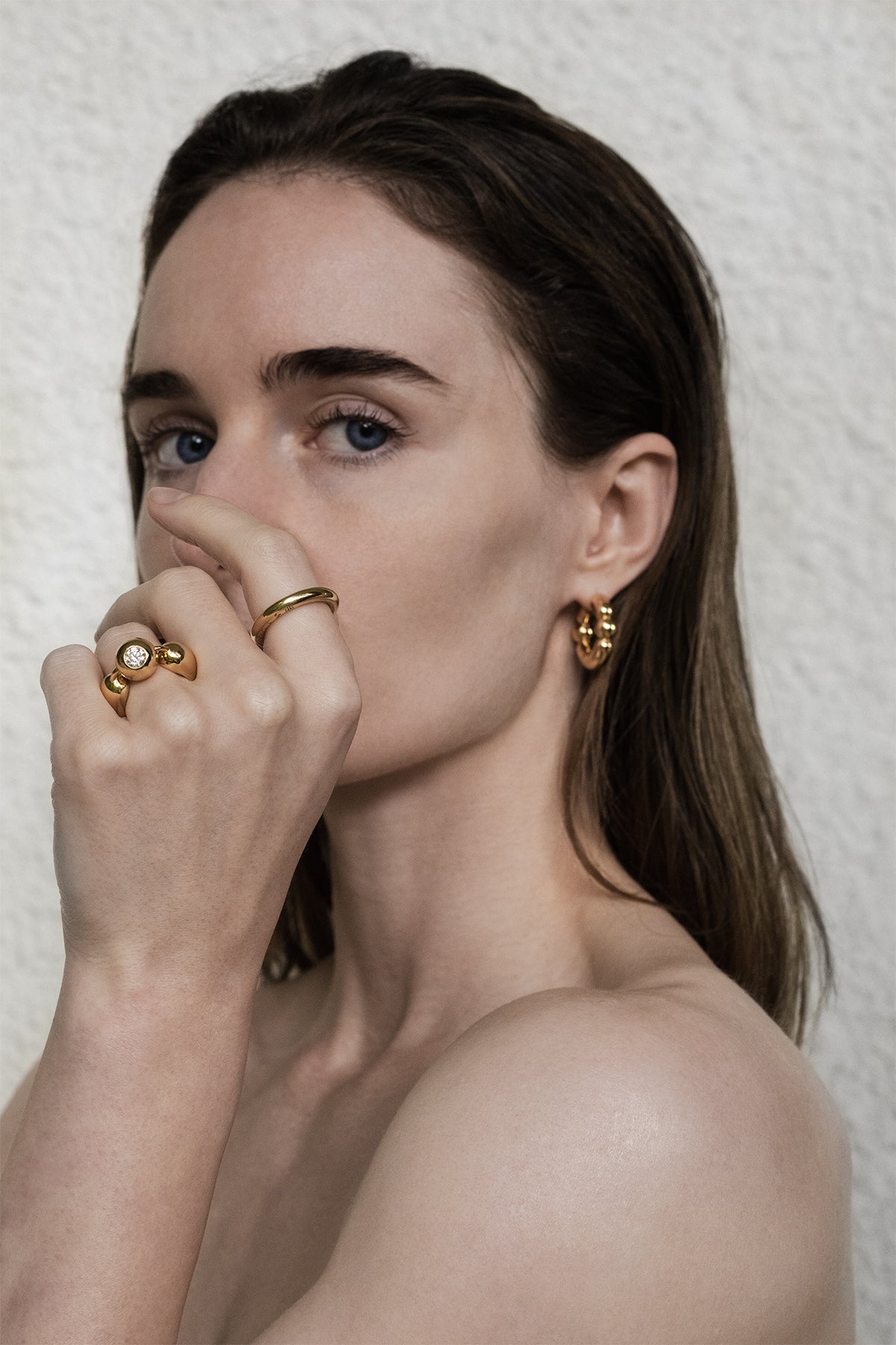 Woman wearing gold jewelry including earrings and rings against a neutral background