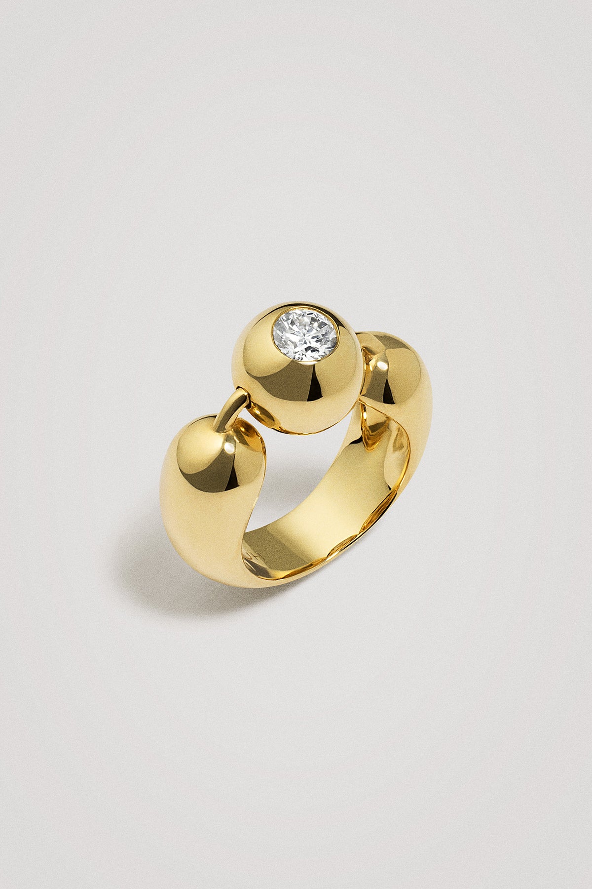 Gold ring with a diamond on a spherical element on a light gray background