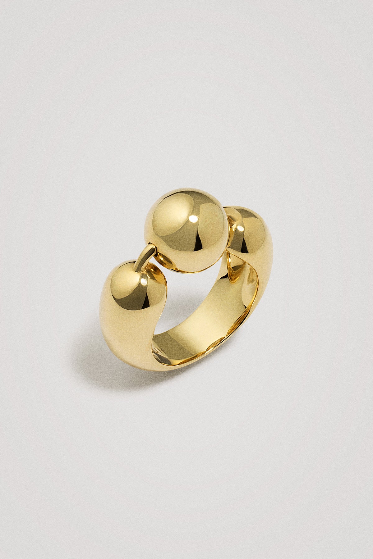 Gold ring with a spherical element on a light gray background
