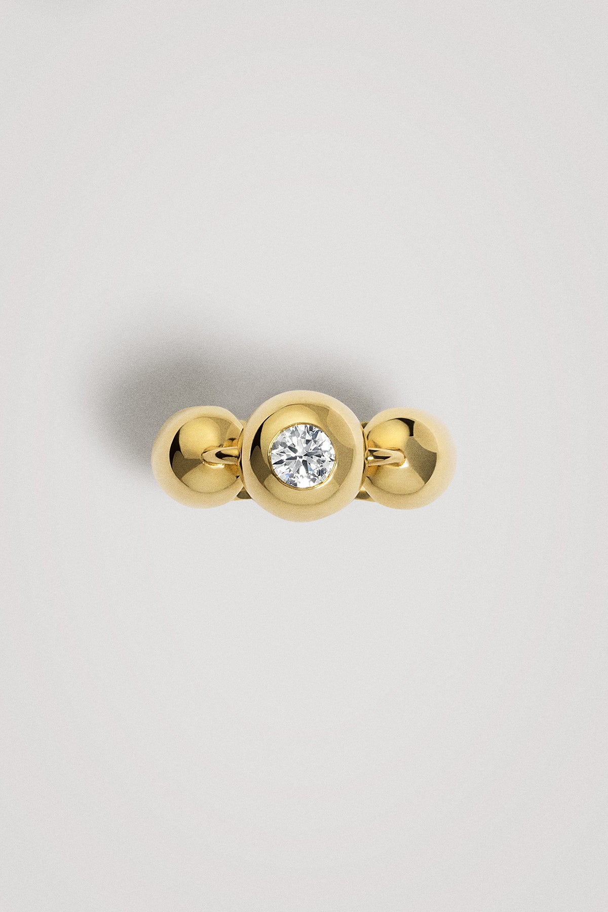 Gold ring with a central diamond on a spherical element on a light gray background