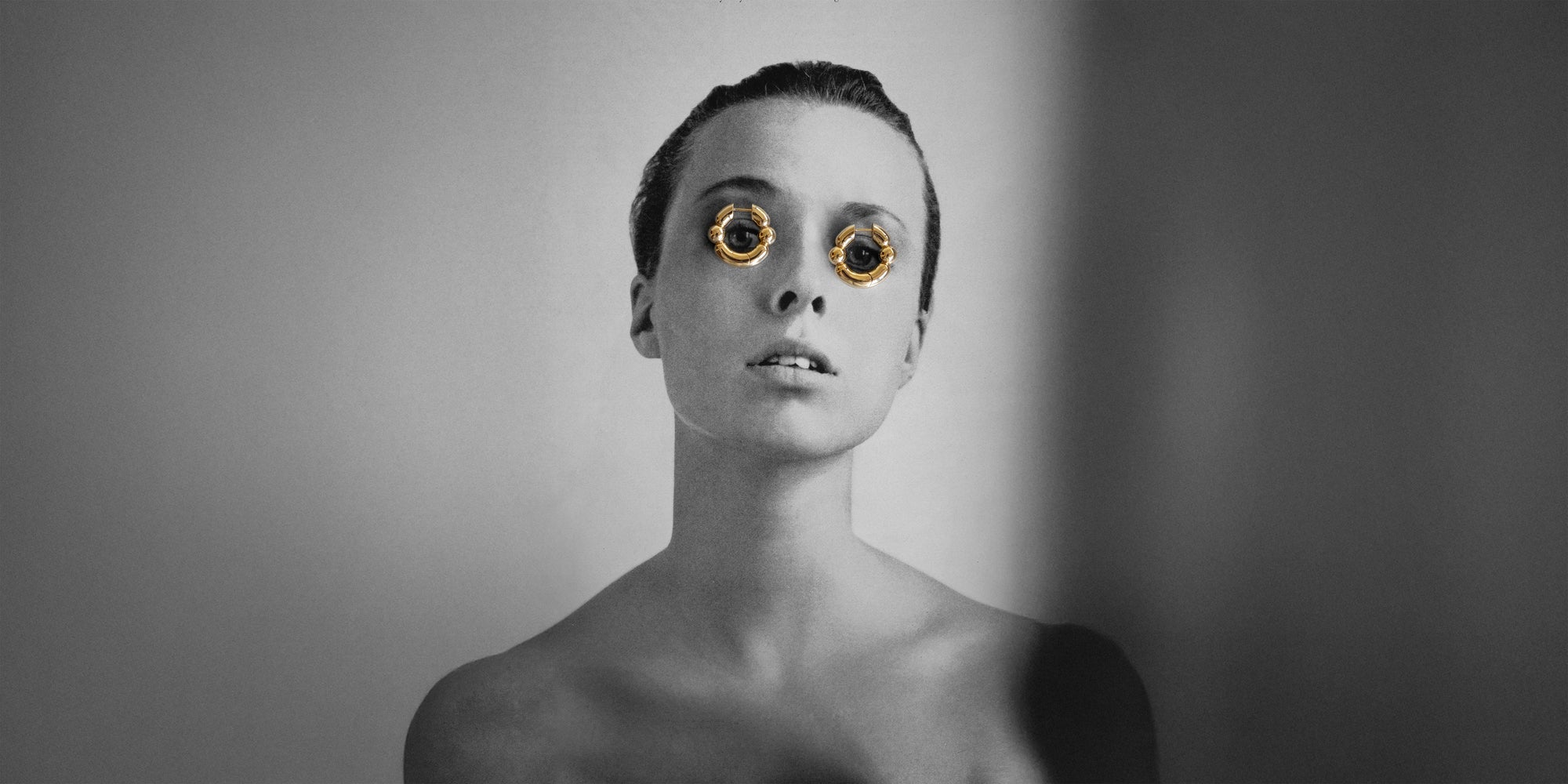 Shapes hoop earrings over the eyes of a black and white vintage Vogue magazine editorial showing a woman with slicked back hair against a white background.