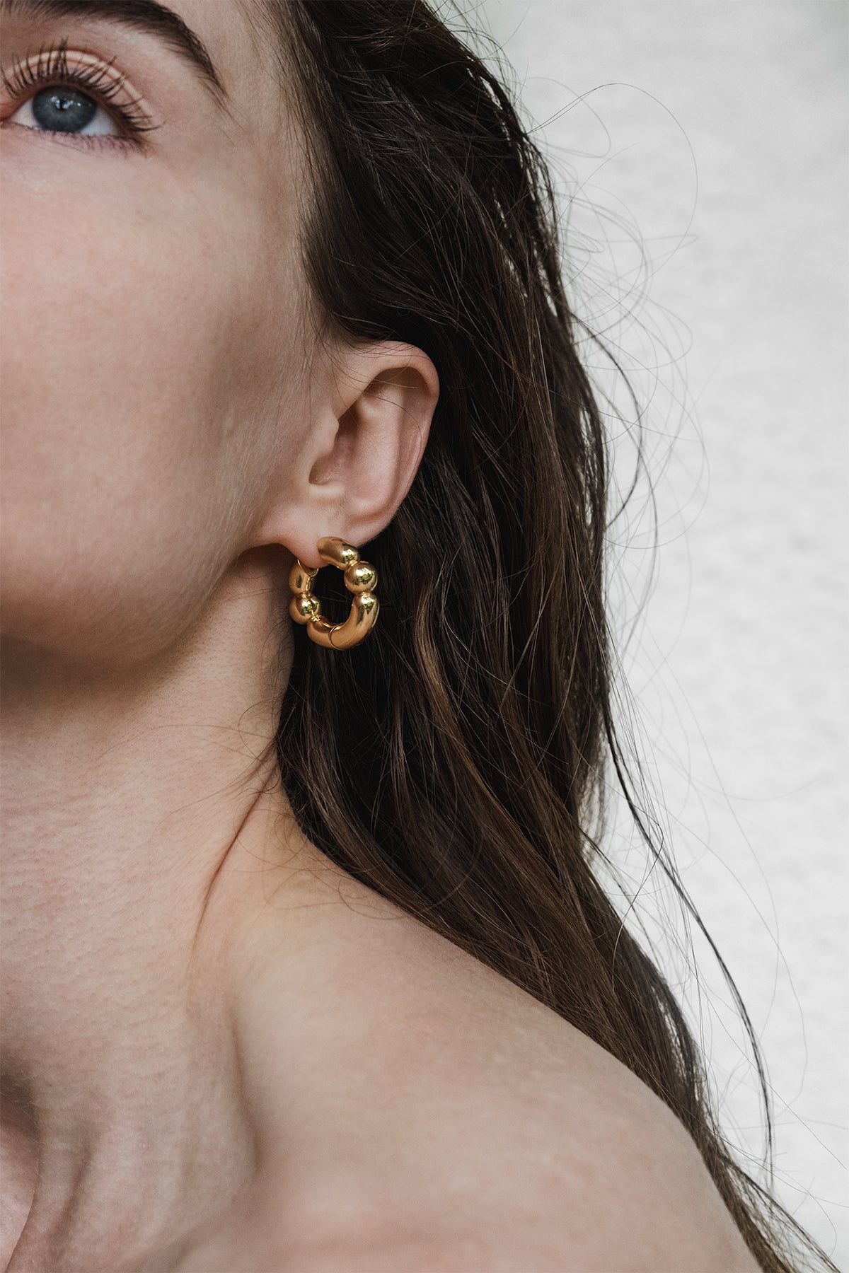 Close-up of a person wearing a gold hoop earring with a neutral background