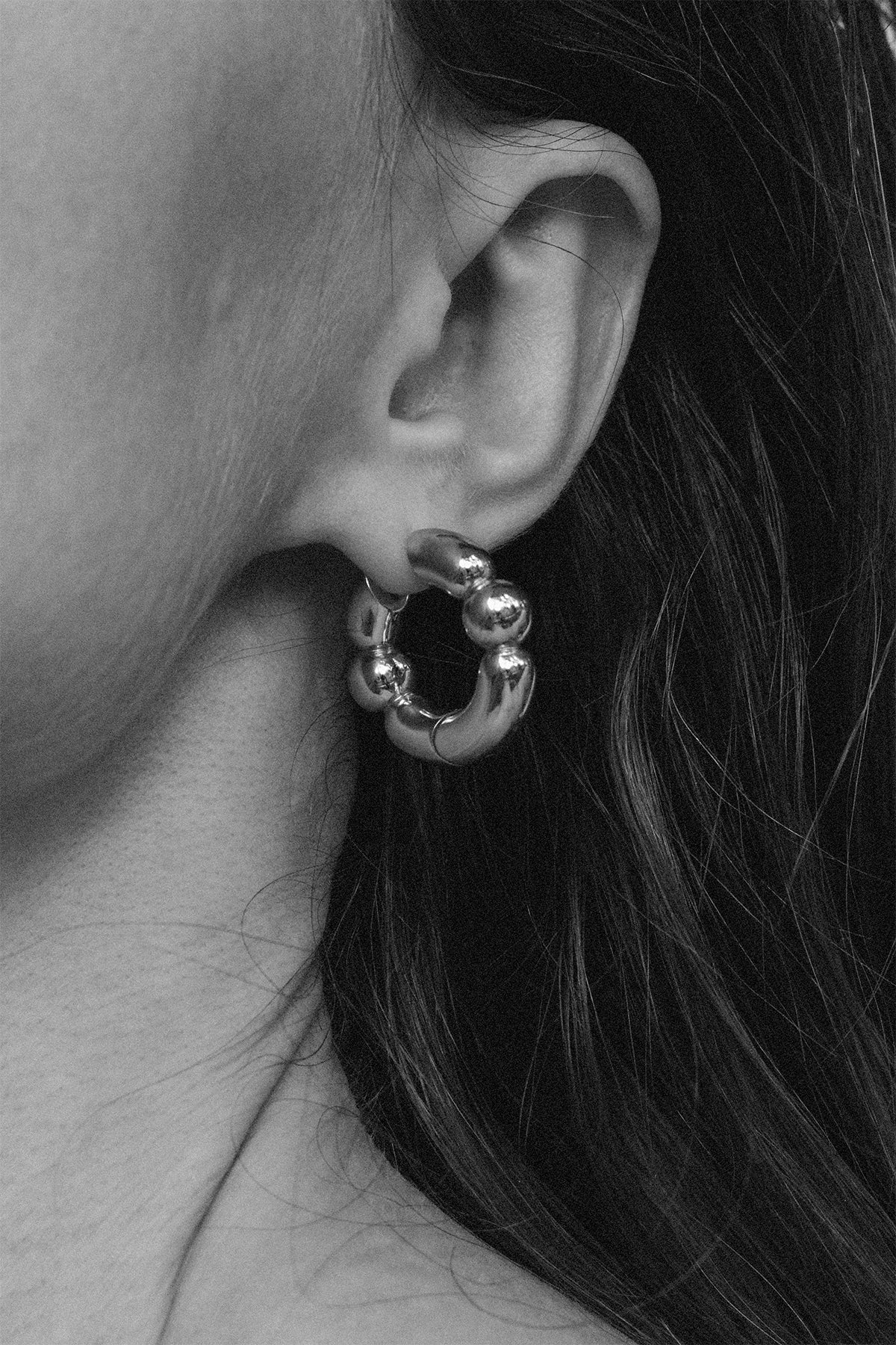 Close-up of a person wearing a gold hoop earring with dark hair.
